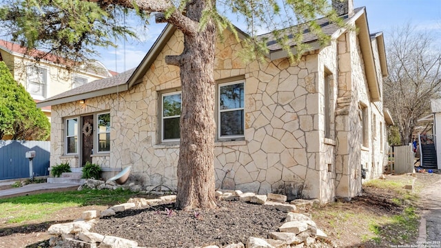 view of side of home with stone siding and fence