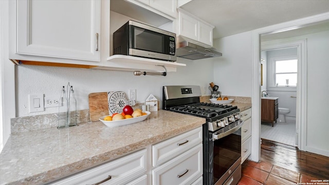 kitchen with under cabinet range hood, white cabinetry, appliances with stainless steel finishes, and wood finished floors