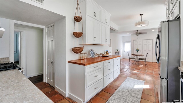 kitchen featuring baseboards, a ceiling fan, wood counters, freestanding refrigerator, and white cabinetry