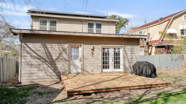 rear view of property featuring french doors, fence, a wooden deck, and solar panels