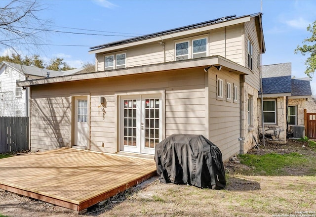 rear view of house with a deck, central AC unit, fence, stone siding, and french doors