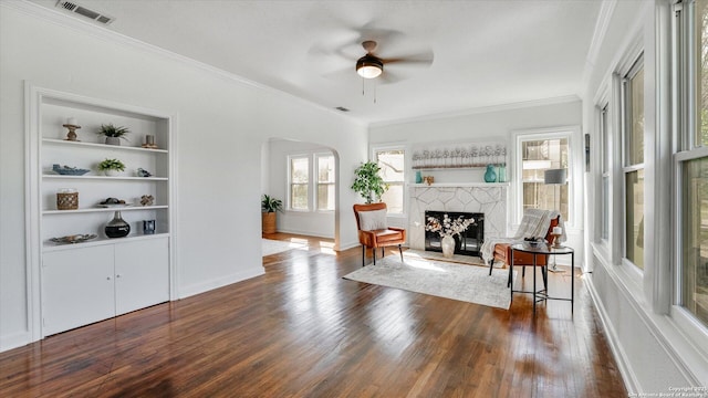 sitting room with arched walkways, a fireplace with raised hearth, visible vents, built in features, and dark wood-style floors