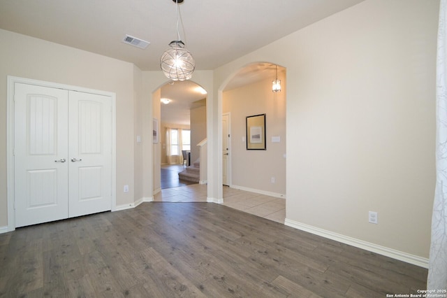 empty room with arched walkways, visible vents, baseboards, and wood finished floors