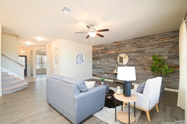 living room featuring arched walkways, an accent wall, wood walls, visible vents, and stairs