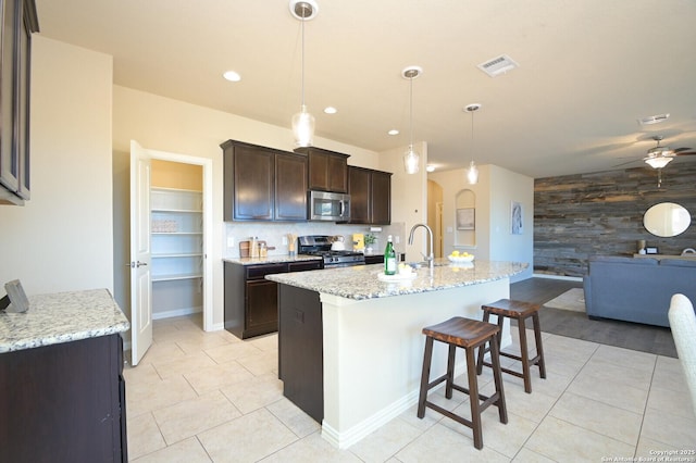 kitchen featuring dark brown cabinetry, an accent wall, wood walls, visible vents, and appliances with stainless steel finishes