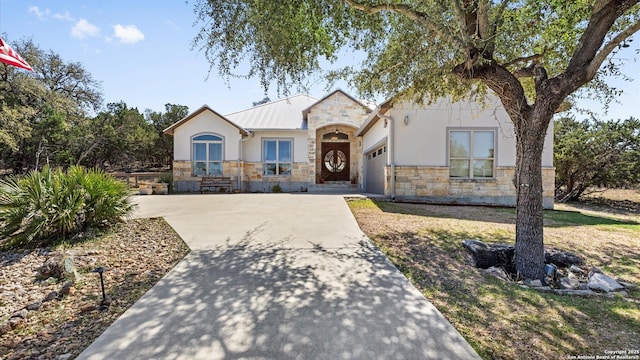 view of front facade with metal roof, an attached garage, stone siding, concrete driveway, and stucco siding