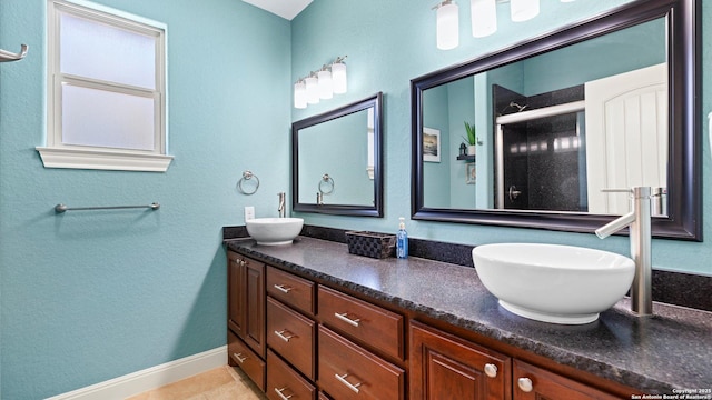 bathroom featuring double vanity, a stall shower, baseboards, and a sink