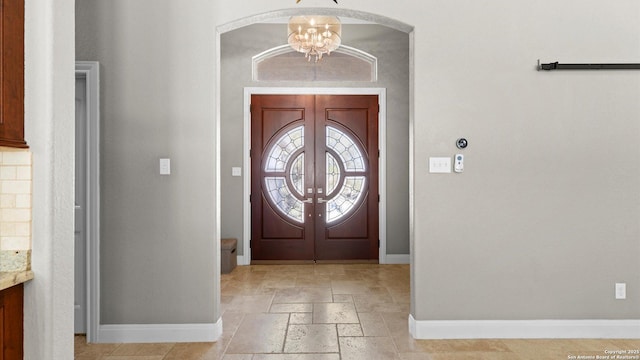 entryway featuring baseboards, french doors, a chandelier, and stone tile floors