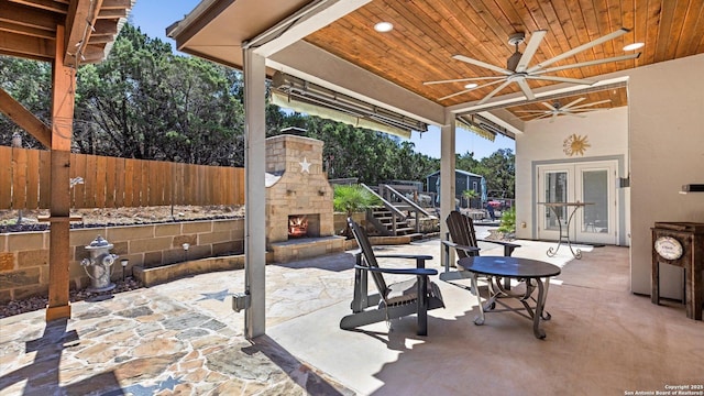 view of patio / terrace with ceiling fan, fence, and an outdoor stone fireplace