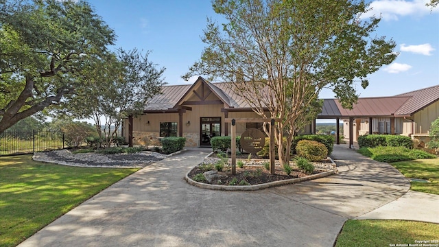 view of front facade with metal roof, fence, stone siding, french doors, and a standing seam roof