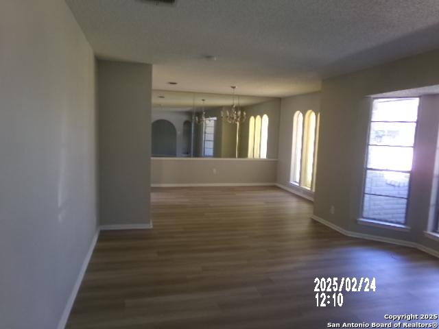 empty room with baseboards, a textured ceiling, a chandelier, and dark wood-type flooring