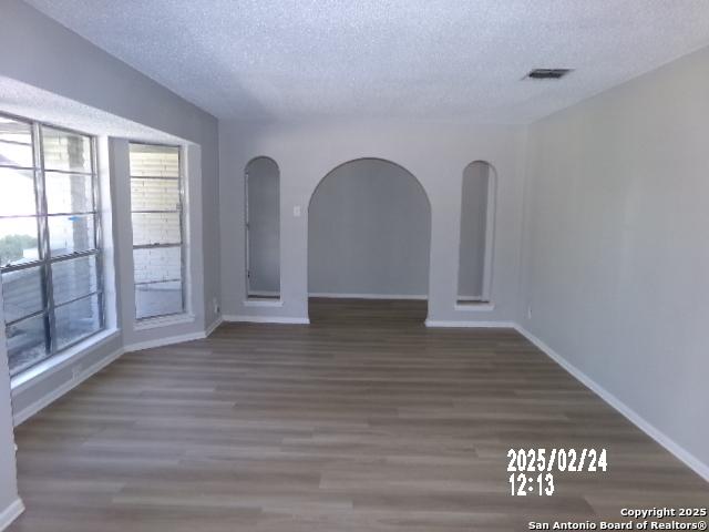 empty room featuring baseboards, visible vents, a textured ceiling, and wood finished floors