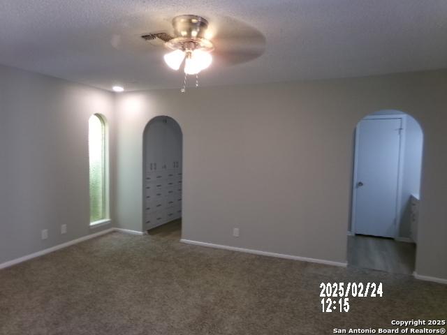 carpeted empty room featuring arched walkways, a ceiling fan, and baseboards