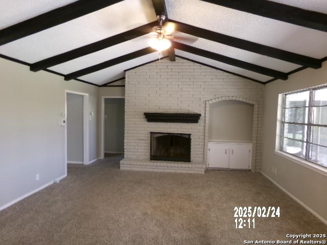 unfurnished living room with vaulted ceiling with beams, a ceiling fan, baseboards, a brick fireplace, and carpet