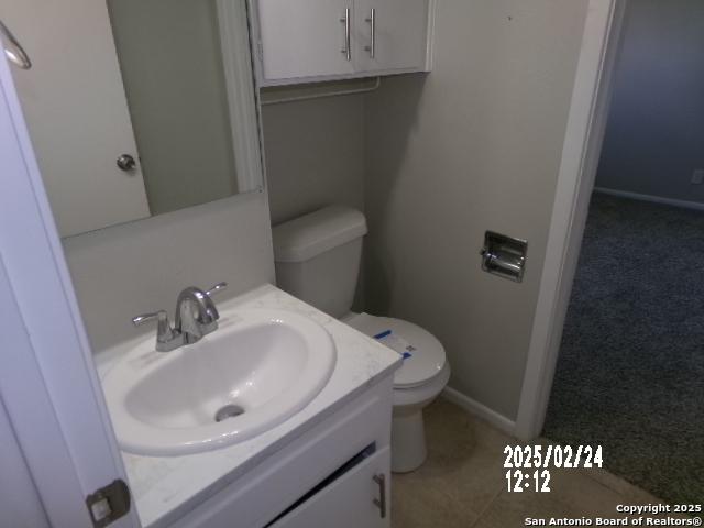 half bathroom with tile patterned flooring, vanity, toilet, and baseboards