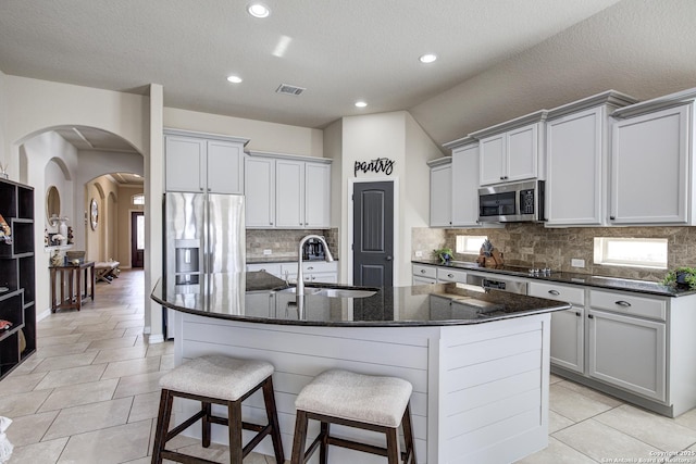 kitchen with arched walkways, a kitchen island with sink, a sink, visible vents, and appliances with stainless steel finishes