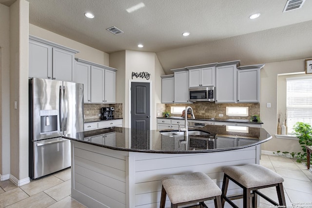 kitchen with tasteful backsplash, visible vents, an island with sink, stainless steel appliances, and a sink