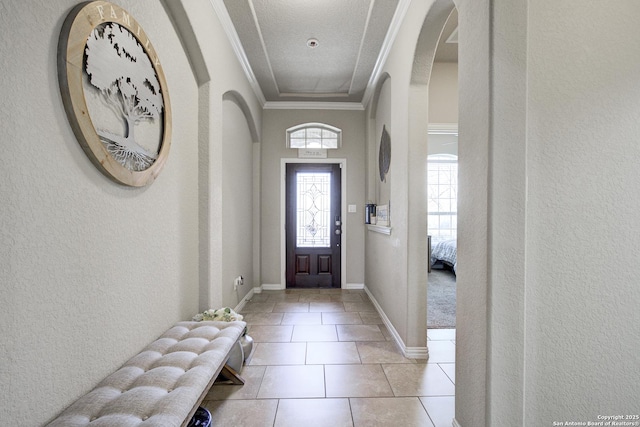 tiled foyer entrance with a textured wall, arched walkways, crown molding, and baseboards