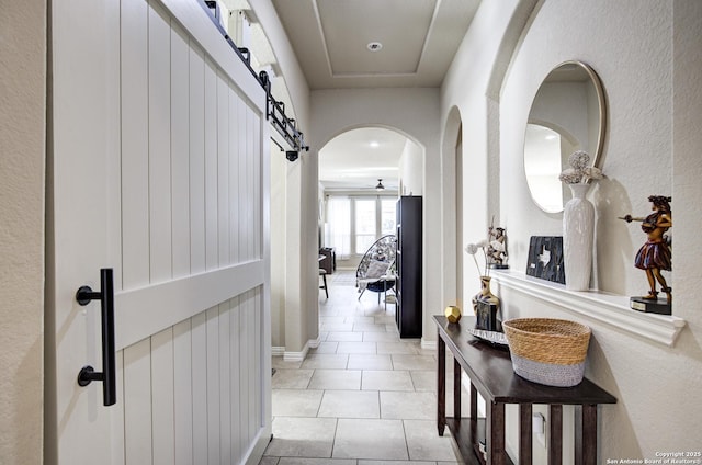 hallway with light tile patterned floors, a barn door, and baseboards