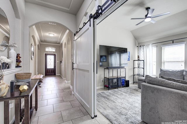 entryway with arched walkways, light tile patterned floors, a barn door, a ceiling fan, and crown molding