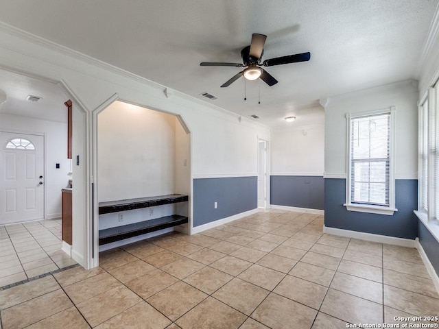 empty room with light tile patterned floors, visible vents, arched walkways, a ceiling fan, and crown molding