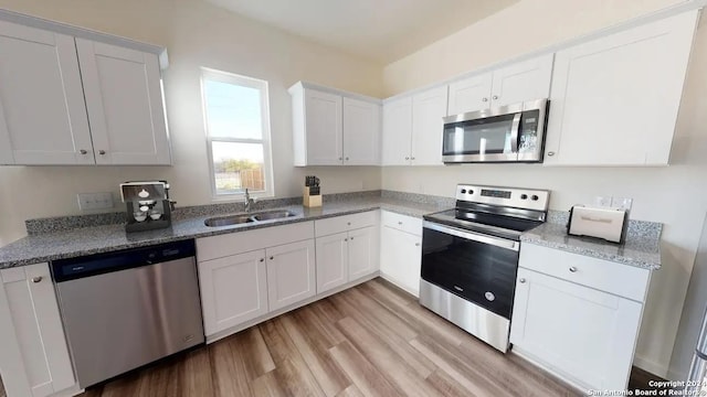 kitchen featuring stainless steel appliances, a sink, white cabinets, light stone countertops, and light wood finished floors