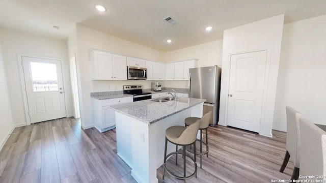 kitchen with stainless steel appliances, white cabinets, light wood-type flooring, a kitchen bar, and a center island with sink