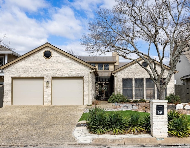 mid-century home with metal roof, a garage, concrete driveway, stone siding, and a standing seam roof