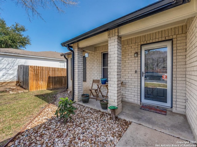 view of exterior entry featuring brick siding and fence