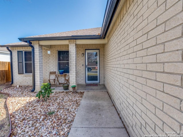 property entrance with covered porch, roof with shingles, fence, and brick siding