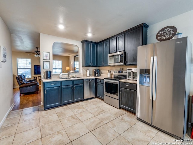 kitchen featuring arched walkways, light tile patterned floors, light countertops, appliances with stainless steel finishes, and a sink