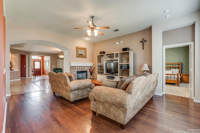 living area with dark wood-style floors, ceiling fan, a fireplace, and arched walkways