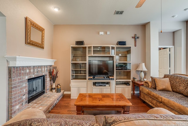 living area featuring visible vents, a ceiling fan, a brick fireplace, wood finished floors, and baseboards