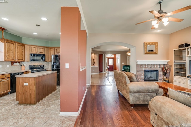 kitchen featuring a fireplace, open floor plan, a center island, black appliances, and tasteful backsplash