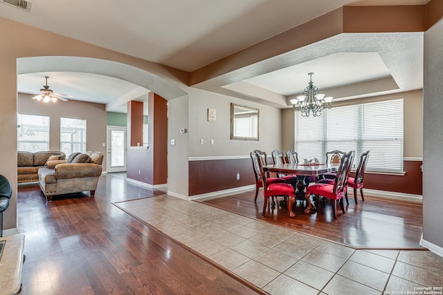 dining space with visible vents, arched walkways, a raised ceiling, baseboards, and hardwood / wood-style flooring