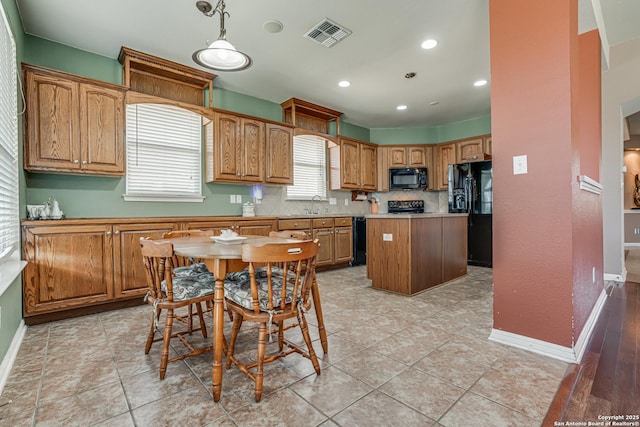 kitchen with baseboards, visible vents, a center island, black appliances, and a sink