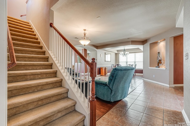 staircase featuring arched walkways, a notable chandelier, a textured ceiling, baseboards, and tile patterned floors