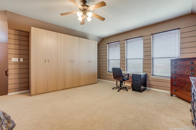 office with a ceiling fan, light colored carpet, vaulted ceiling, and wooden walls