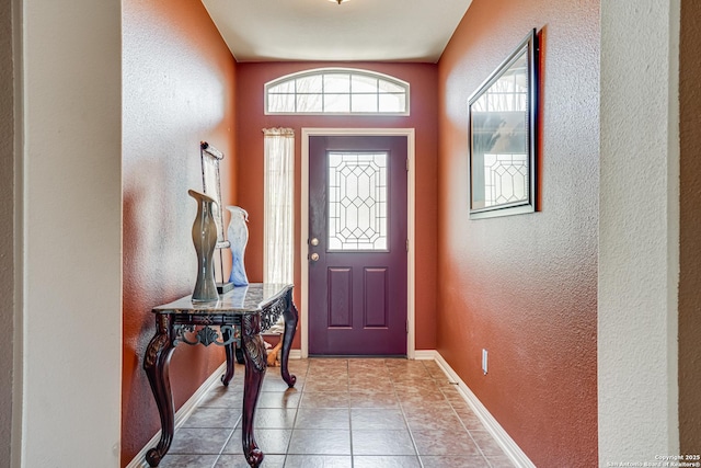 entrance foyer featuring light tile patterned floors, a textured wall, and baseboards