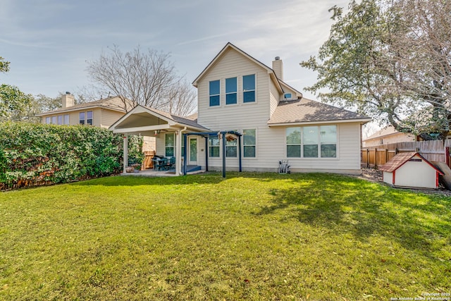 back of property with a yard, a chimney, a patio, a shingled roof, and fence