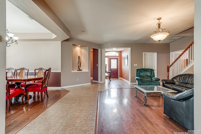 living area with stairs, a notable chandelier, wood finished floors, and baseboards