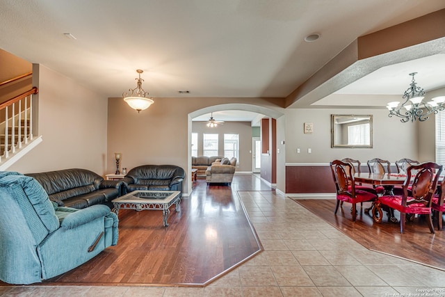 tiled living area featuring visible vents, arched walkways, baseboards, stairway, and a chandelier