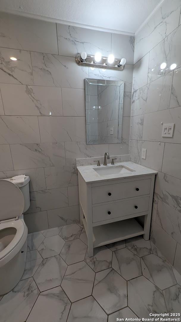 half bathroom featuring toilet, marble finish floor, tile walls, and vanity