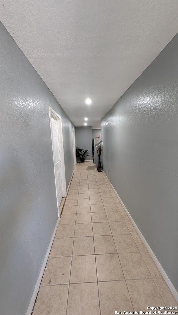 hallway with light tile patterned floors, a textured wall, a textured ceiling, and baseboards