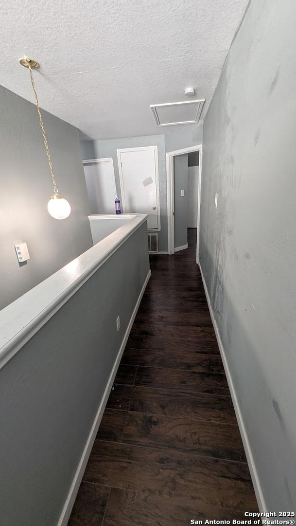 corridor featuring dark wood-style flooring, visible vents, a textured ceiling, and baseboards