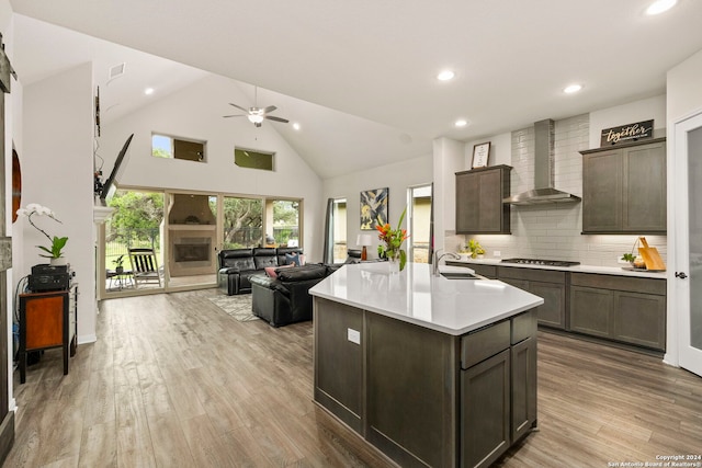 kitchen with a fireplace, a sink, open floor plan, light countertops, and wall chimney range hood