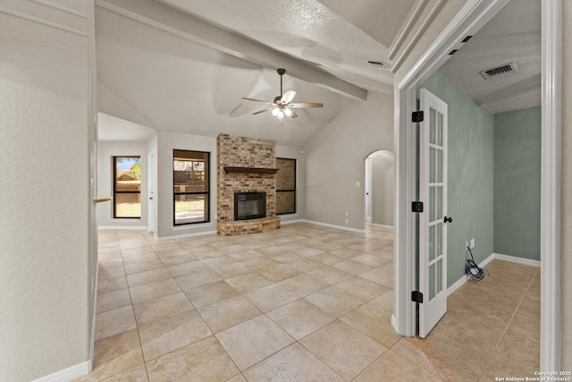 unfurnished living room featuring a ceiling fan, lofted ceiling with beams, a textured ceiling, arched walkways, and a fireplace