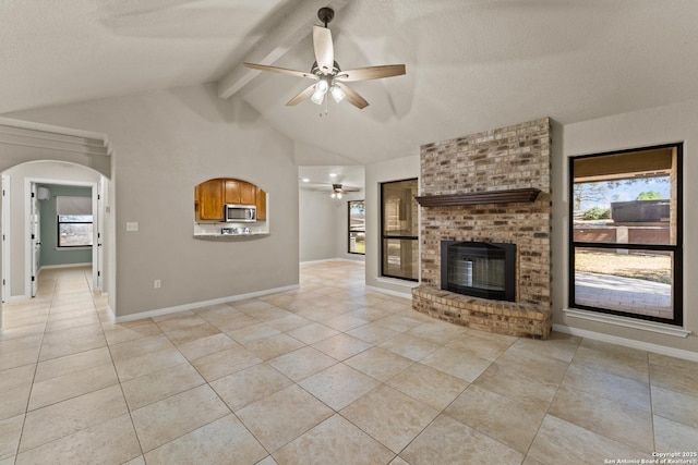 unfurnished living room featuring baseboards, vaulted ceiling with beams, light tile patterned flooring, ceiling fan, and a brick fireplace