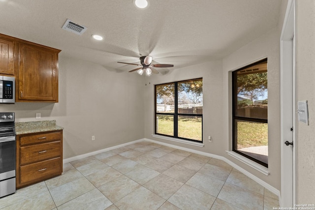 kitchen with visible vents, baseboards, ceiling fan, light stone countertops, and stainless steel appliances