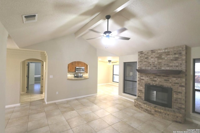 unfurnished living room with visible vents, arched walkways, lofted ceiling with beams, a textured ceiling, and a brick fireplace